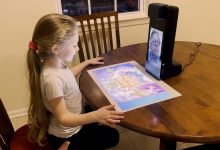 A child sits at a table and looking at a game projected from an Amazon Glow